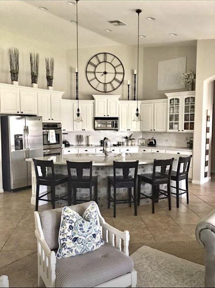 Tall dried pampas grass stems in vases, a round wall clock and black candlesticks arranged above white kitchen cabinets
