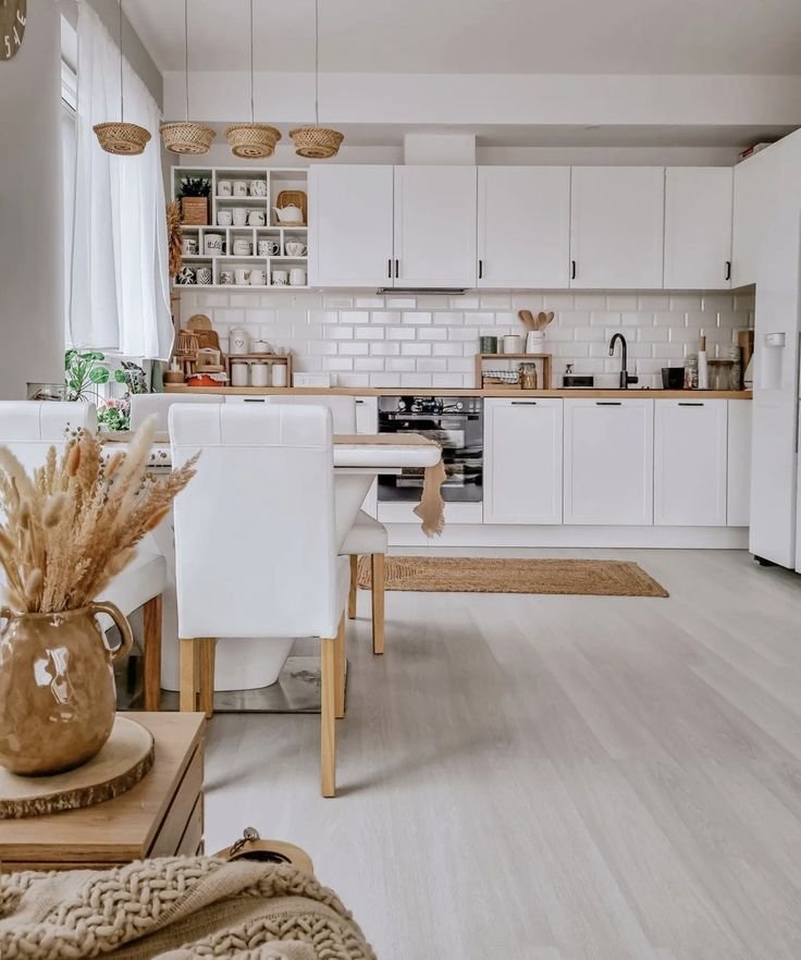 Open white kitchen with bare cabinets and no decor above them, with woven pendant lights and a dining area nearby