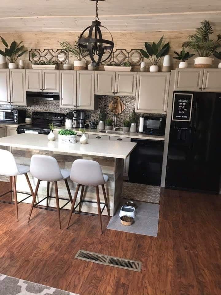Above-cabinet styling with mirrors, candlesticks and trailing plants above white kitchen cabinets around a kitchen island with a chandelier