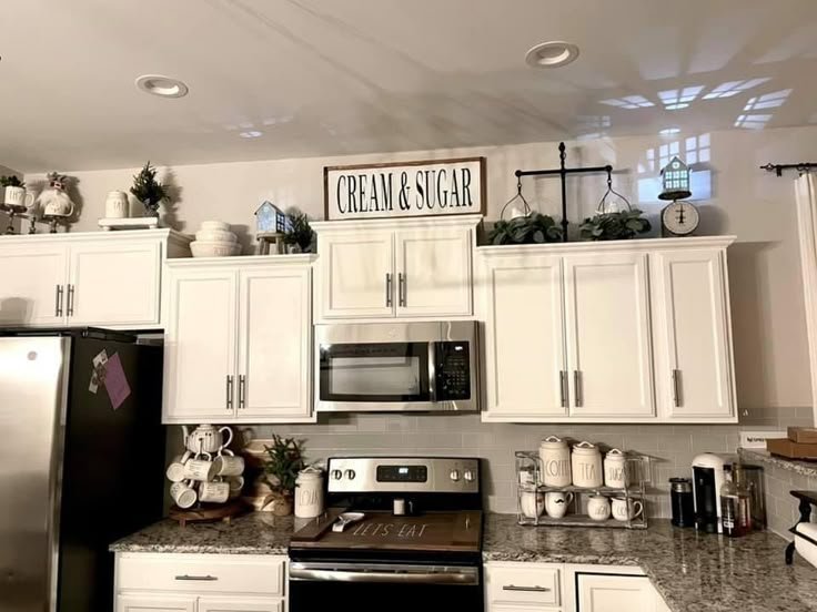 Above-cabinet decor with a woven basket, greenery, framed signs and a lantern above cream kitchen cabinets