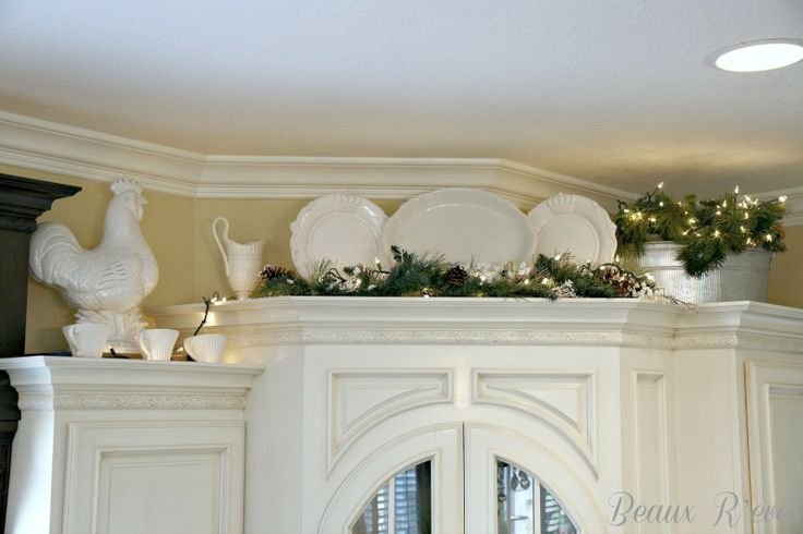 White ceramic rooster figure, a pitcher and greenery with string lights arranged above white kitchen cabinets