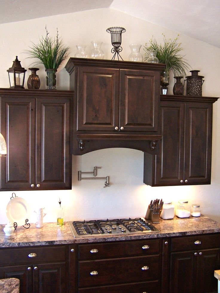 Vintage lanterns, clear glass vases and trailing greenery arranged above dark wood kitchen cabinets