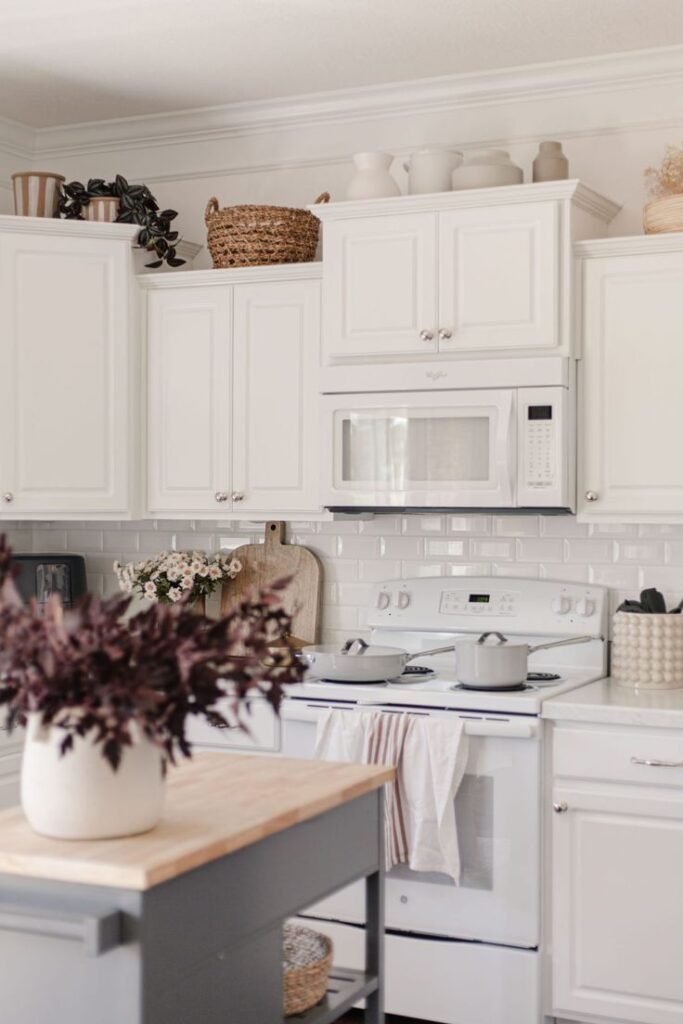 Large woven basket and neutral ceramic vases arranged above white kitchen cabinets with a trailing plant