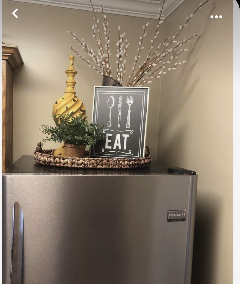 Woven tray styled with an EAT sign, a decorative finial and pussy willow branches above a refrigerator