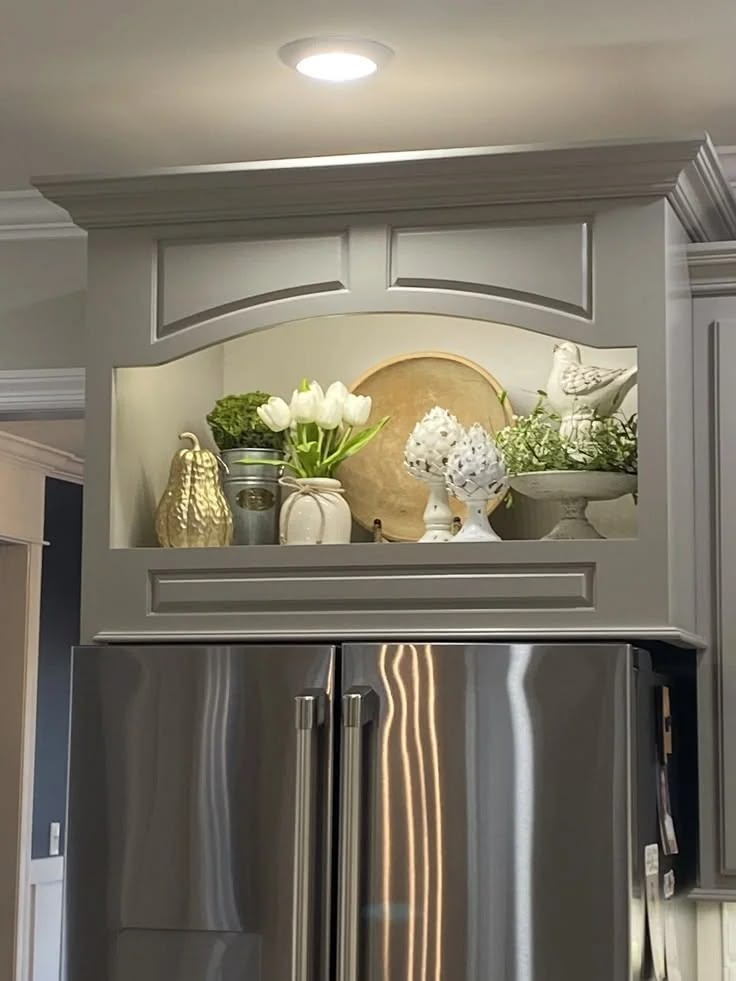 Built-in cabinet niche above a refrigerator styled with tulips, a wood tray and a ceramic bird in neutral tones