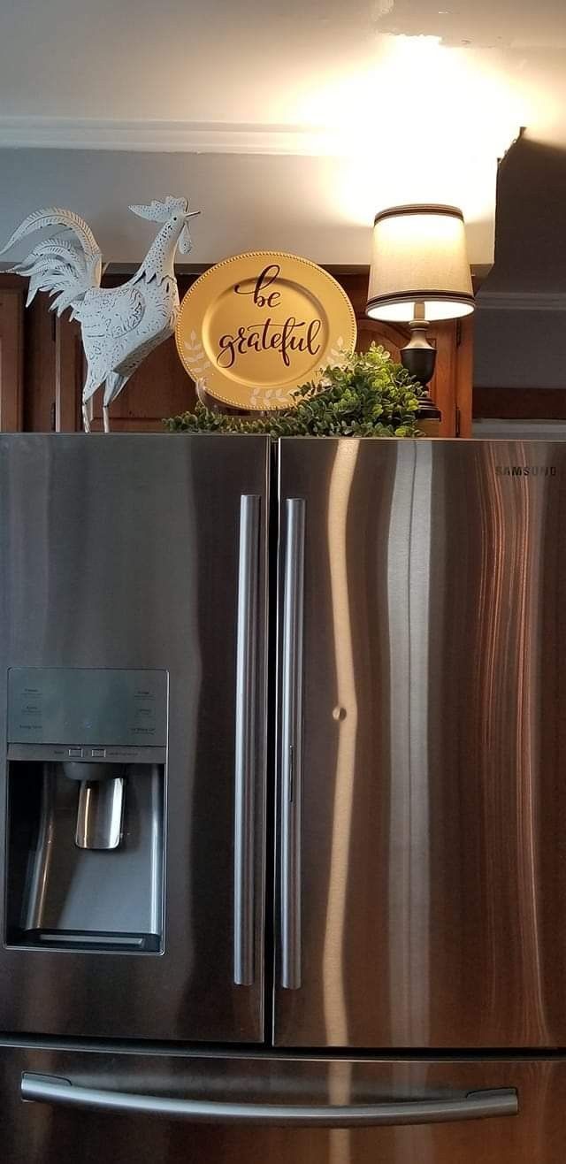 White rooster figurine and a decorative plate styled above a stainless steel refrigerator