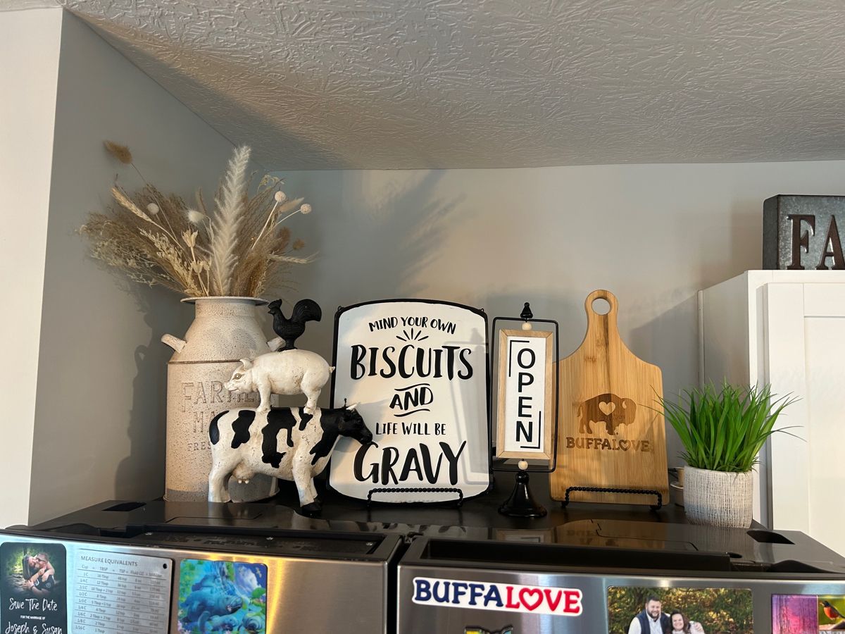 Refrigerator top crowded with farmhouse figurines, signs and a dried floral arrangement