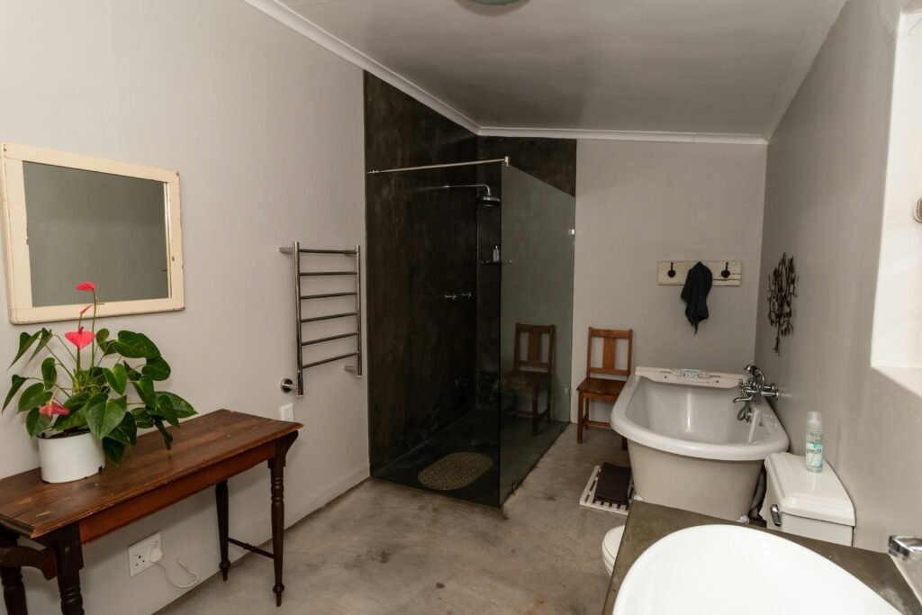 Wall-mounted hook holding a dark towel beside a freestanding chrome towel warmer and a glass-walled shower stall