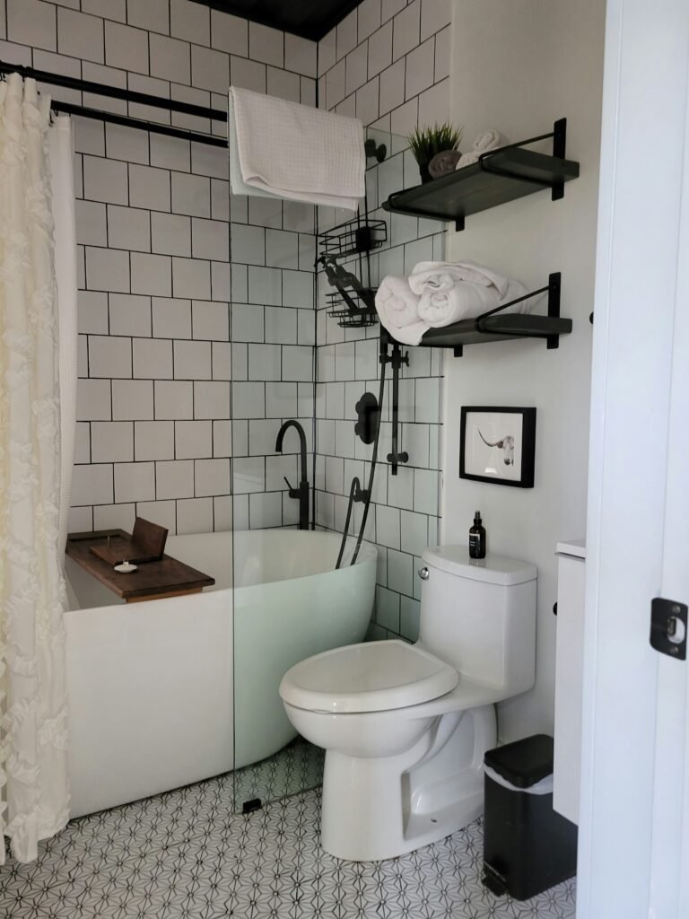Black floating shelves above a tub holding rolled white towels, a small potted plant and a framed art print