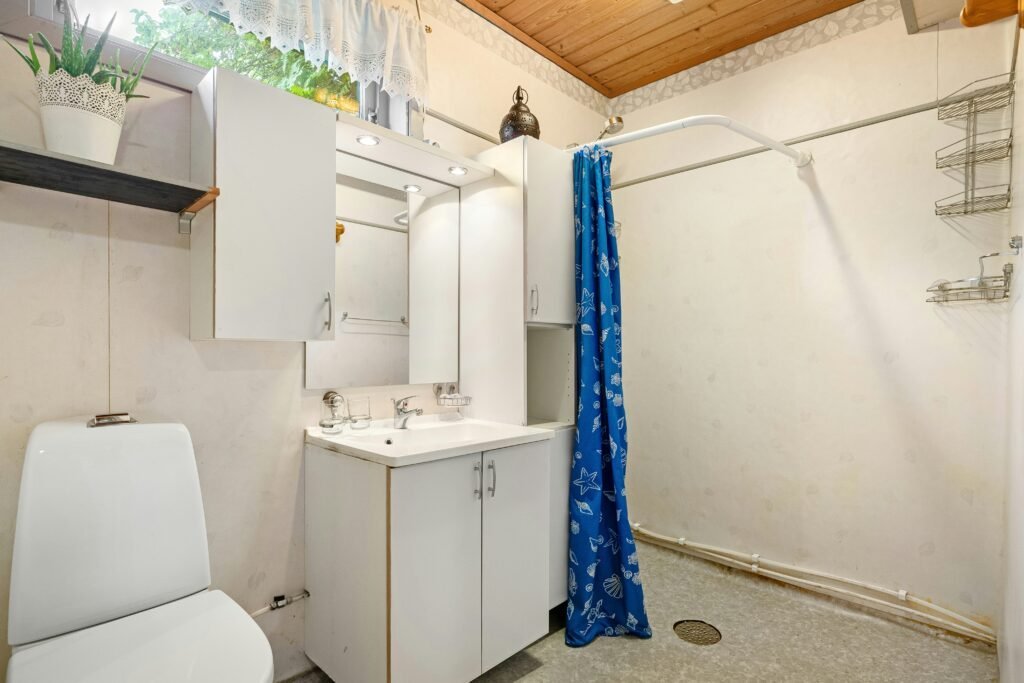White bathroom vanity with closed cabinet doors and a mirror beside a toilet and a blue seashell-print shower curtain