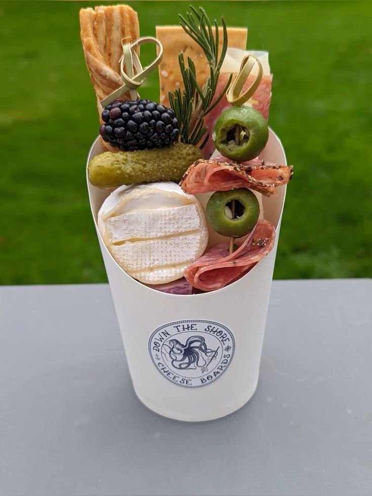 Portable mini picnic charcuterie cup with cheese, meat and a breadstick, set outdoors on grass