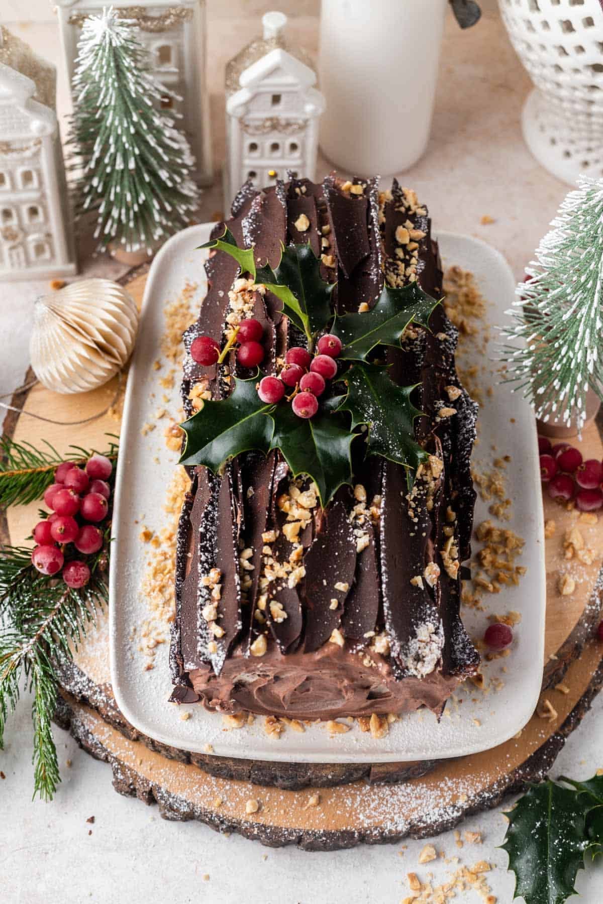 A chocolate yule log cake with chocolate bark shavings, holly, and red berries on top