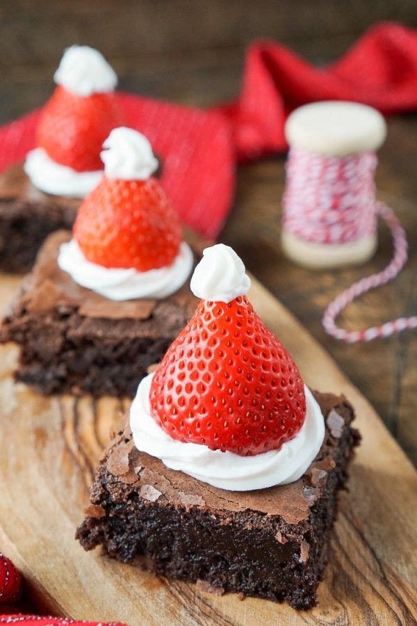 Chocolate brownies topped with whipped cream and a strawberry shaped like a Santa hat