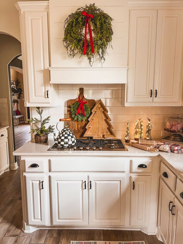 A greenery wreath hanging from a wood tree cutting board on a stove backsplash