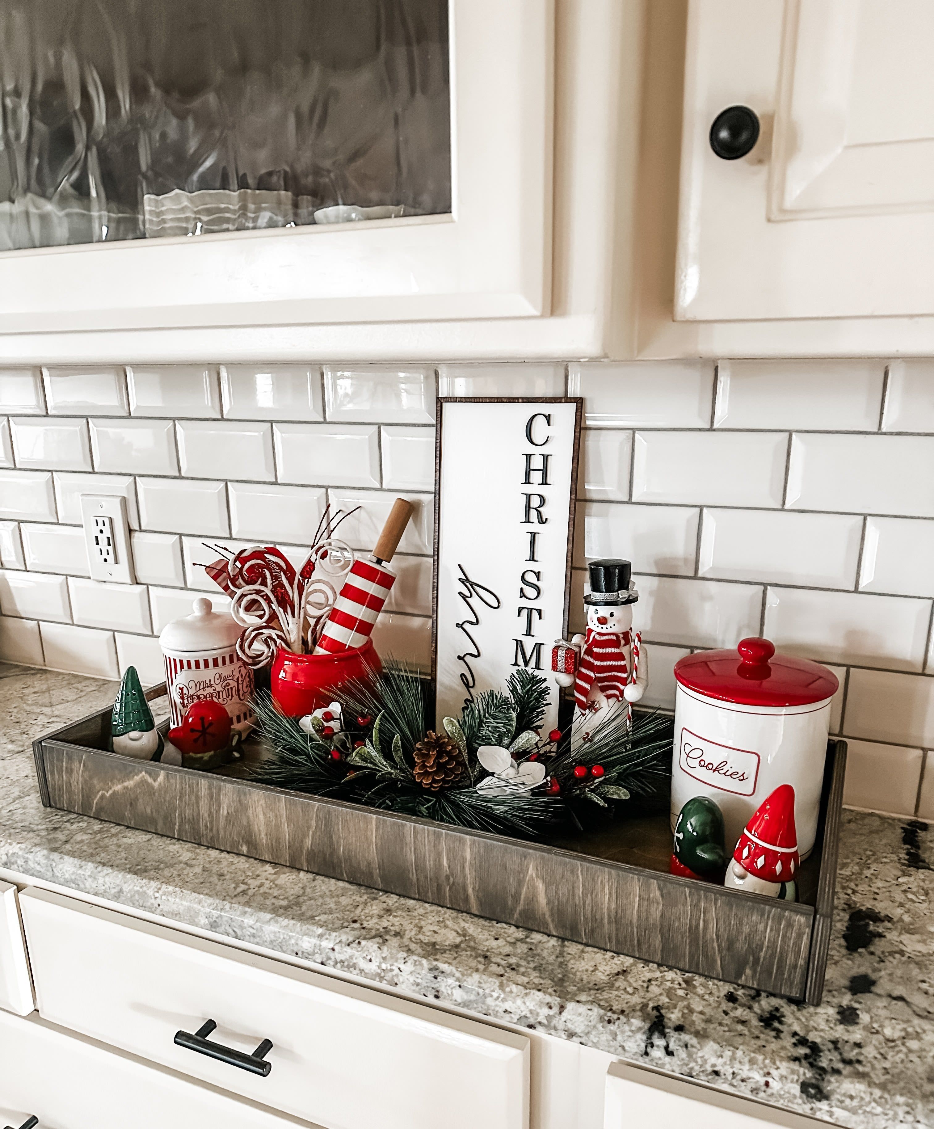 A wooden tray with gnomes, a snowman jar, and a vertical Merry Christmas sign