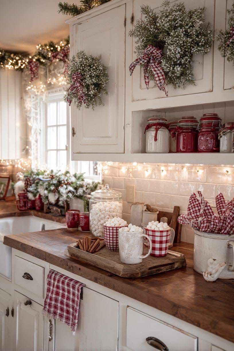 Baby's breath wreaths tied with plaid bows hanging on white upper kitchen cabinets above a butcher-block counter with cocoa mugs