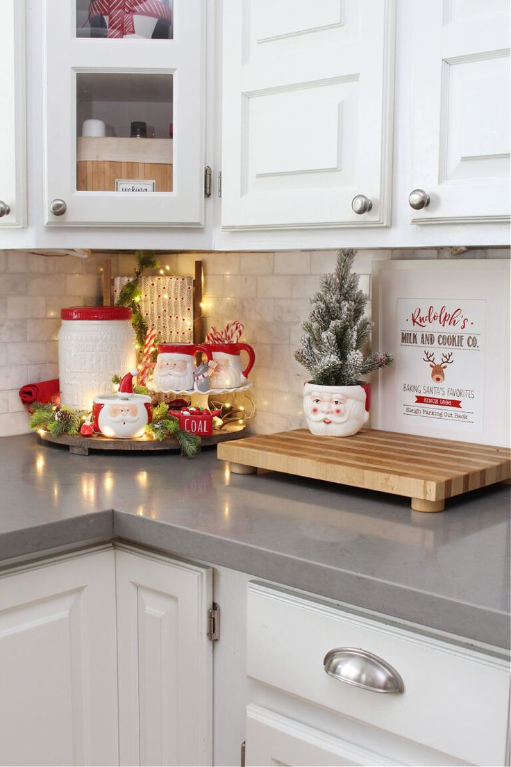Tiered rack of Santa face mugs, candy canes and a coal dish on a gray counter beside a wood cutting board with a Santa planter