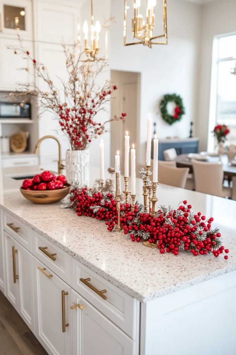 A red berry and brass candlestick runner down a white kitchen island