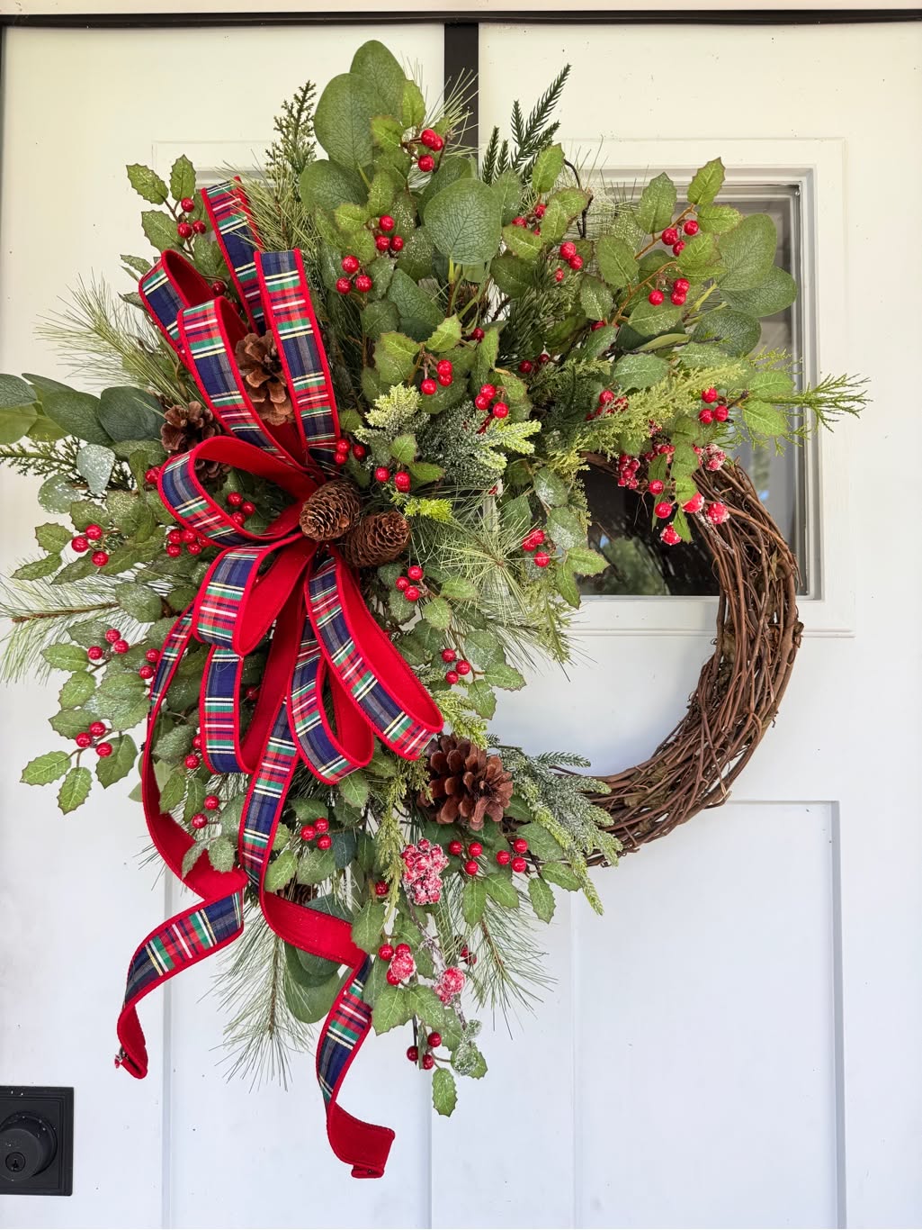 Eucalyptus and berry wreath with a red and navy tartan bow on a white door