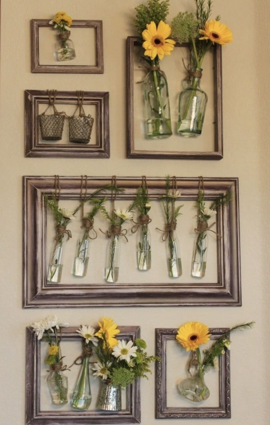 Wall of wooden frames holding small glass bottles filled with fresh daisies, sunflowers and herbs