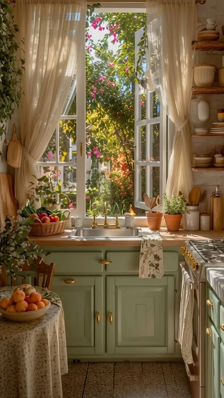 Sage green cottage kitchen with an open window above the sink, potted herbs on the sill and a flowering garden visible outside
