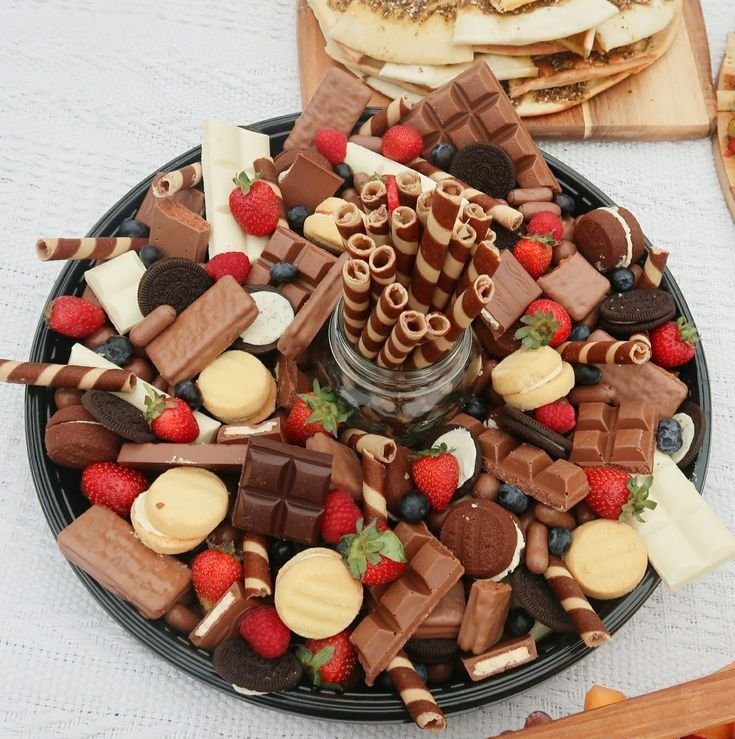 Round chocolate dessert board with chocolate bars, strawberries, Oreos, chocolate chip cookies and chocolate wafer rolls