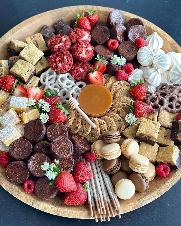 Round dessert board with cookies, brownies, strawberries, macarons, pretzel sticks and caramel dip arranged by color
