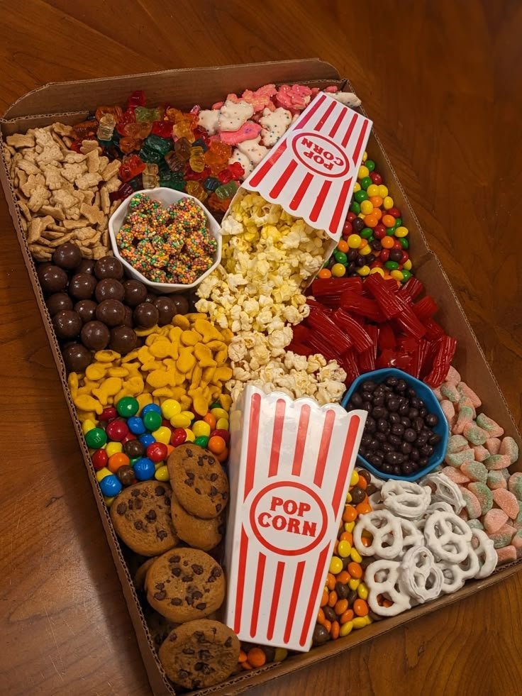 Movie night dessert board with popcorn in paper boxes, gummy bears, chocolate pretzels, cookies, M&Ms and licorice