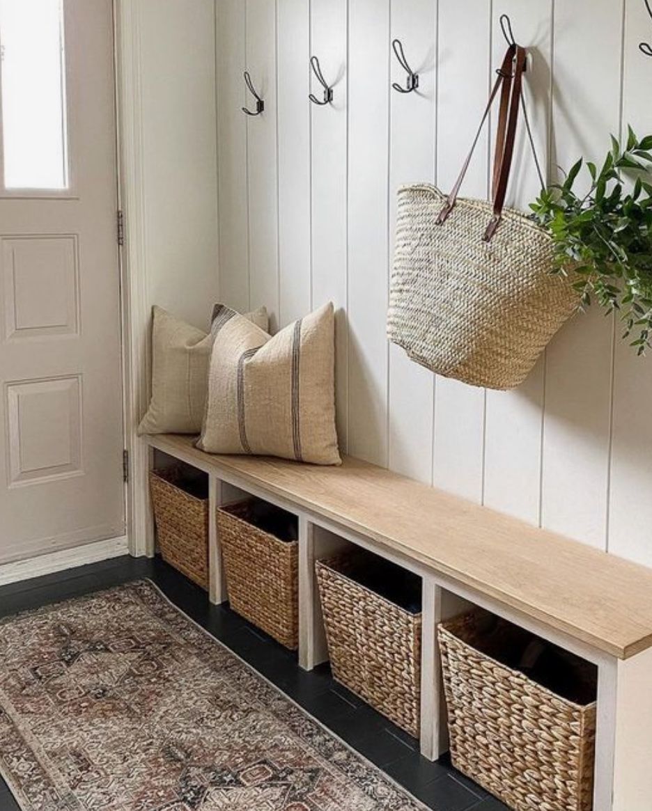 A vertical plank wall with black hooks, a straw tote and a long bench with four baskets