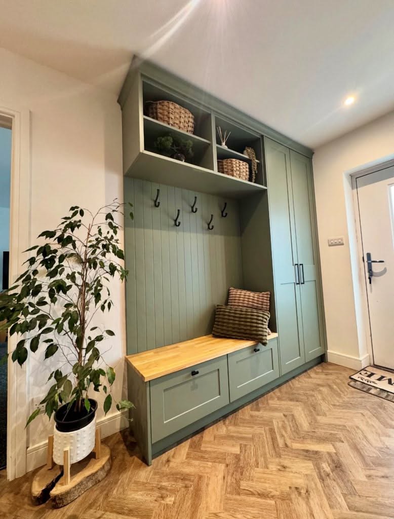 A sage green mudroom built-in with a wood bench seat, two drawers and tall cabinet doors
