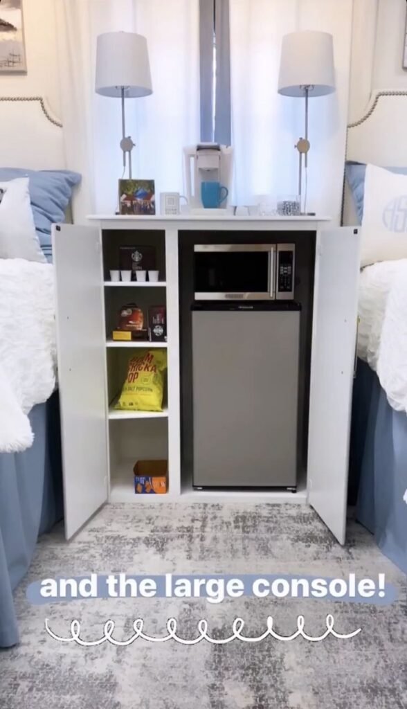 White dorm room console with doors open revealing a mini-fridge and microwave, a coffee maker and two lamps on top between two beds