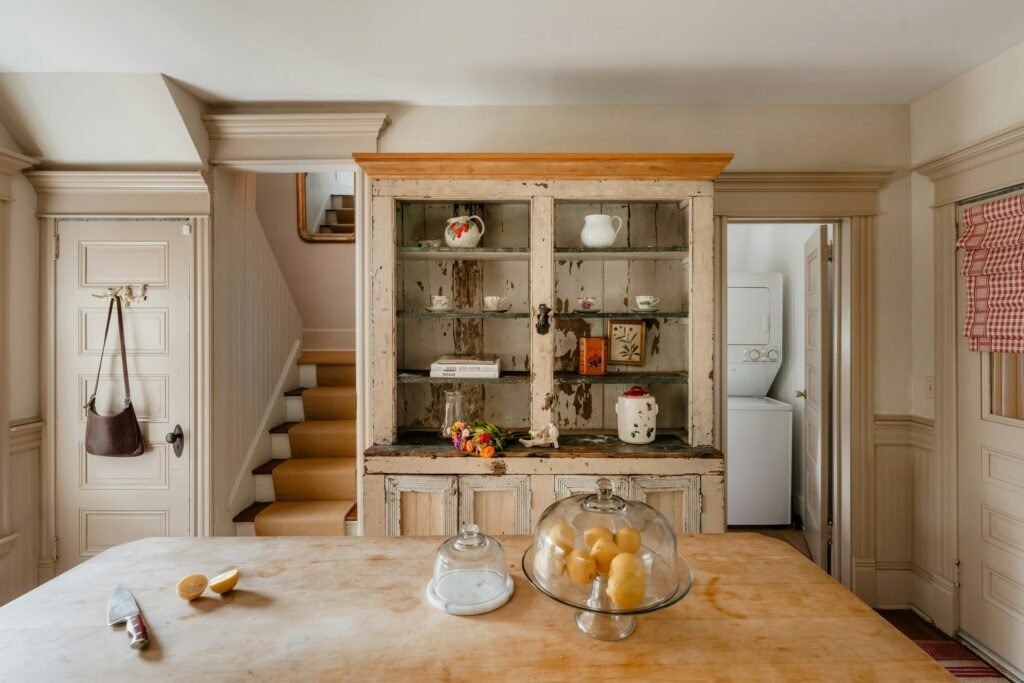 Antique chippy white-painted wood hutch cabinet with vintage latch hardware and glassware, beside a worn wood table