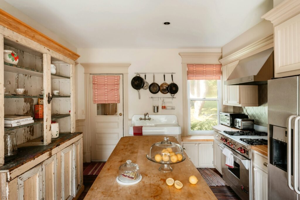 Worn wood kitchen island with hanging pots above, a vintage white hutch and a farmhouse sink in the background