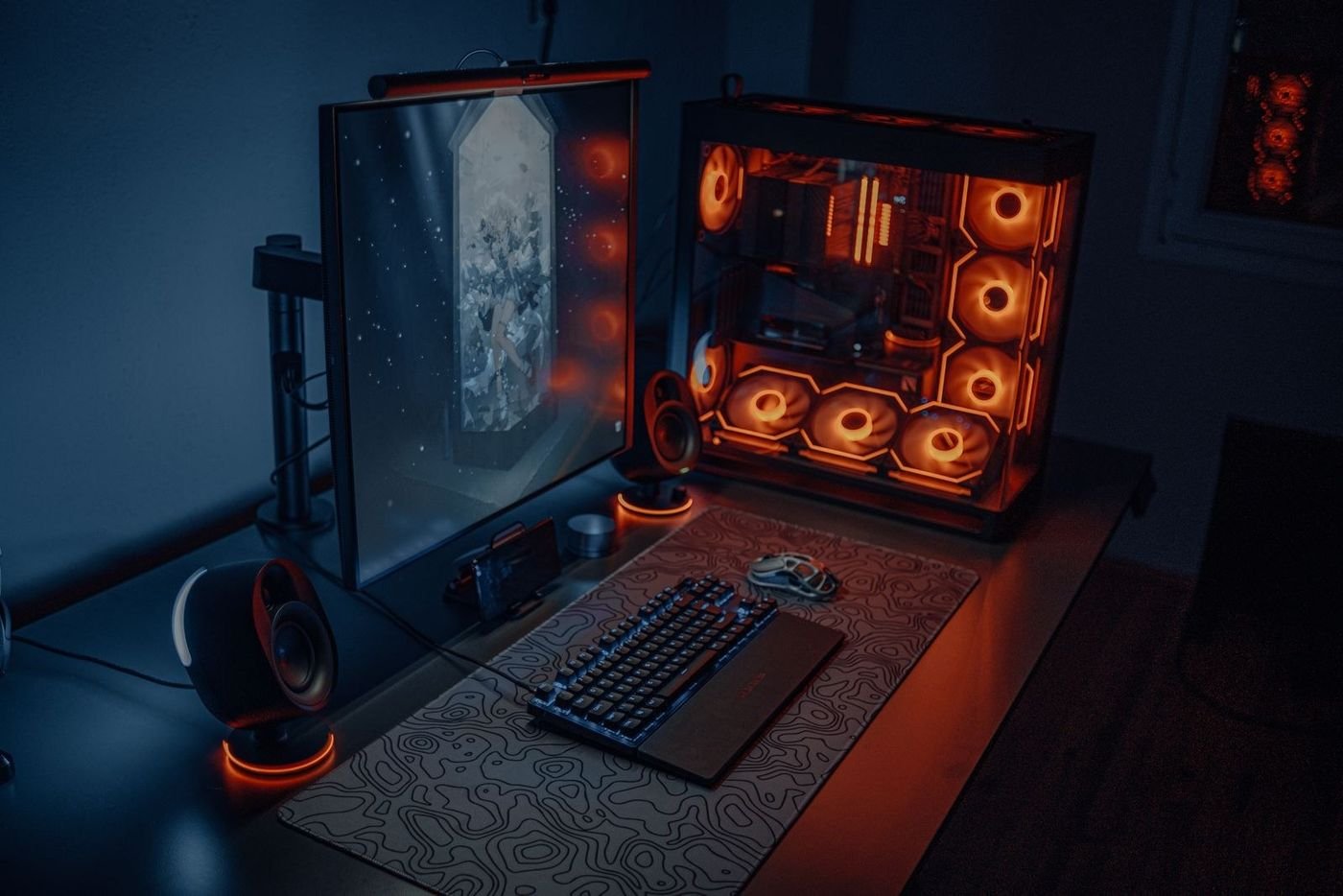 Dual monitor RGB gaming desk setup glowing orange and red with a mechanical keyboard and speakers in a dark room