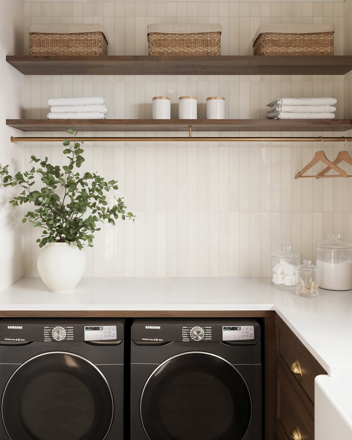 Vertical subway tile backsplash behind a washer and dryer with a brass hanging rod and wood shelves