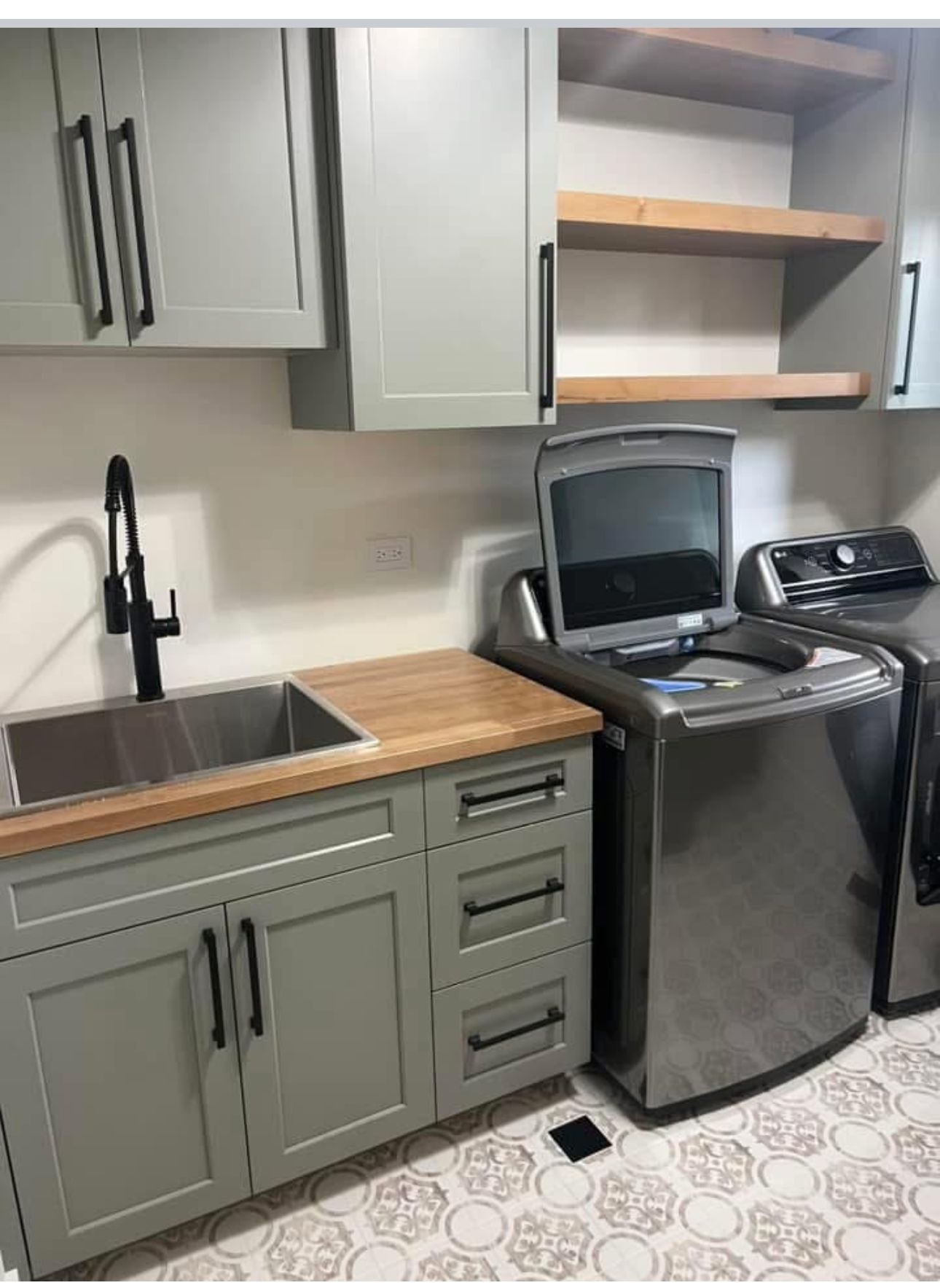 Laundry room utility sink with a black gooseneck faucet and sage green cabinetry
