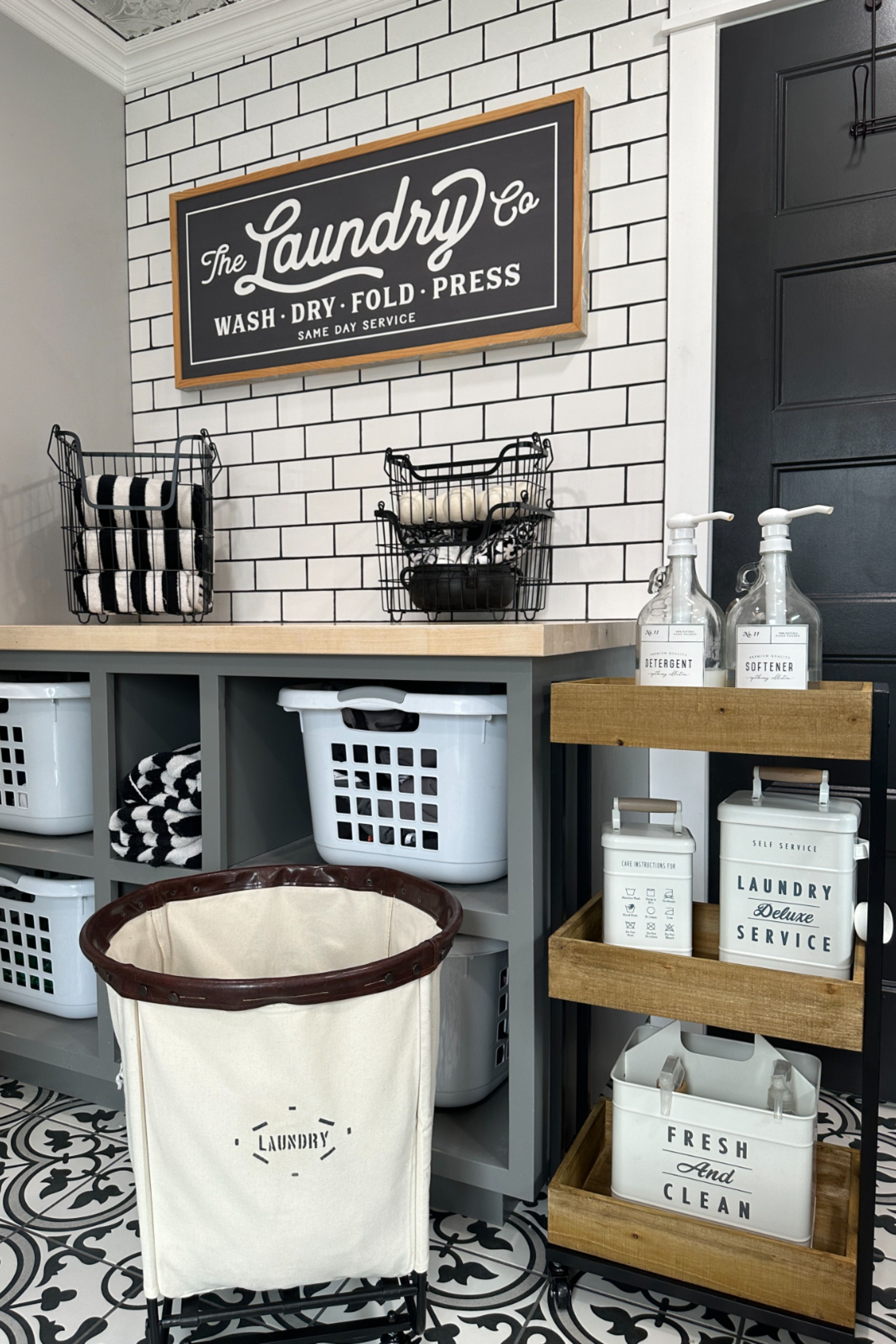 The Laundry Co wash dry fold press sign above open cubbies holding laundry baskets and a canvas hamper