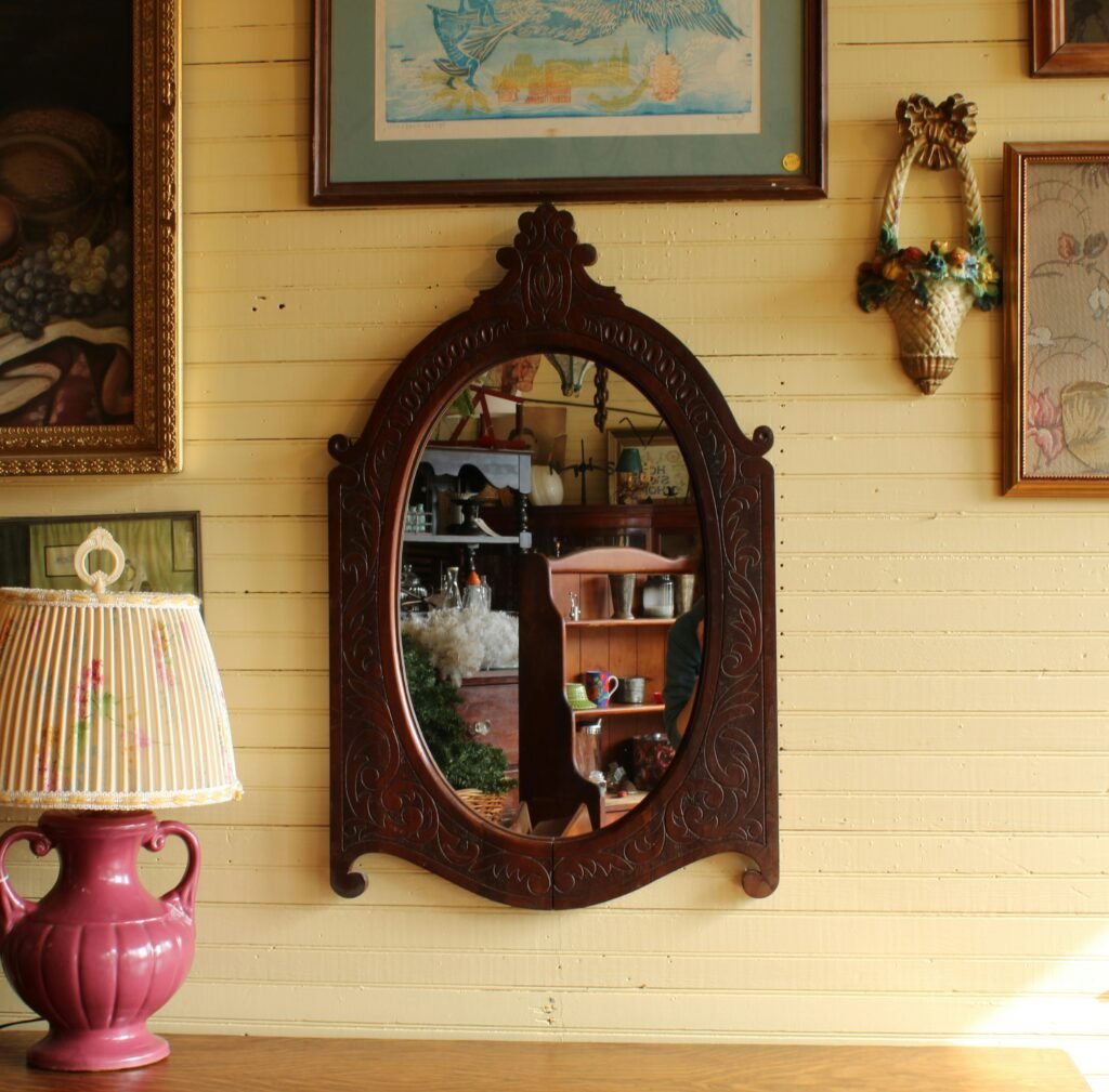 Ornate carved wood-framed antique mirror with a softly mottled finish on a vintage gallery wall