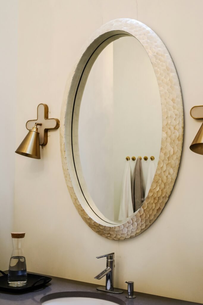Oval scalloped-frame mirror above a bathroom vanity with brass sconces on either side
