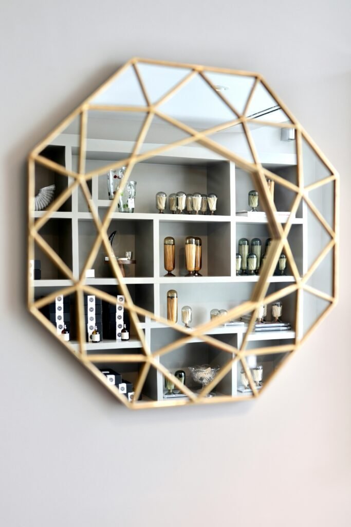 Geometric faceted mirror with gold line details reflecting a styled display shelf