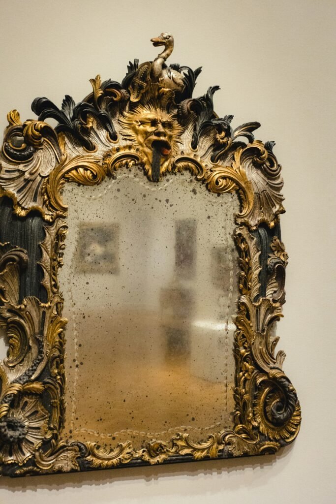 Ornate antique mirror frame mixing gold and dark carved details with a softly aged mirror finish