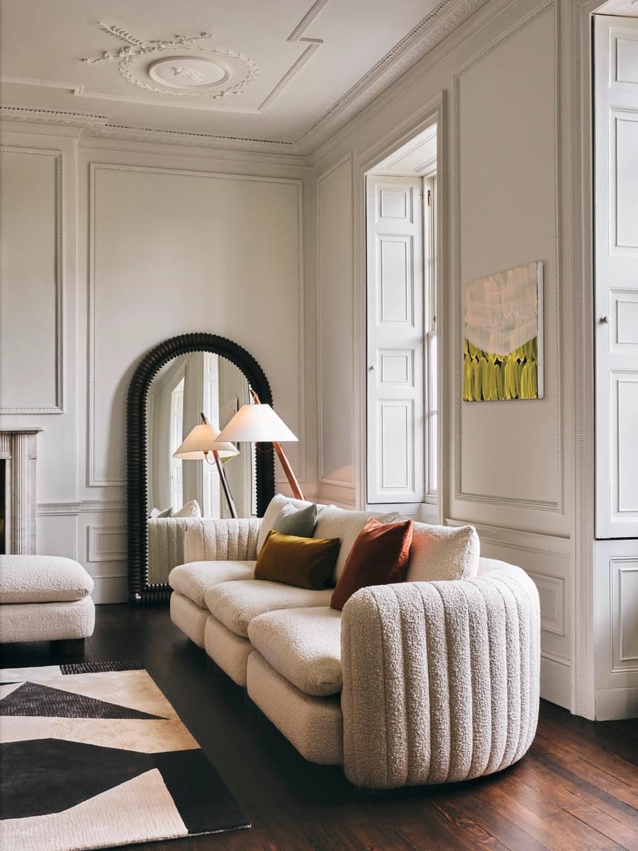 Cream bouclé sofa with vertical channel tufting on a curved arm in a paneled room with an arched mirror