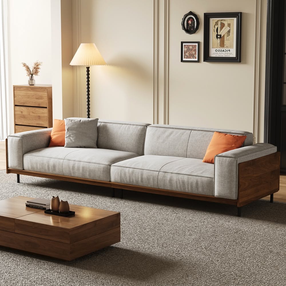 Light gray sofa with a walnut wood frame and orange pillows beside a wood coffee table and a pleated floor lamp