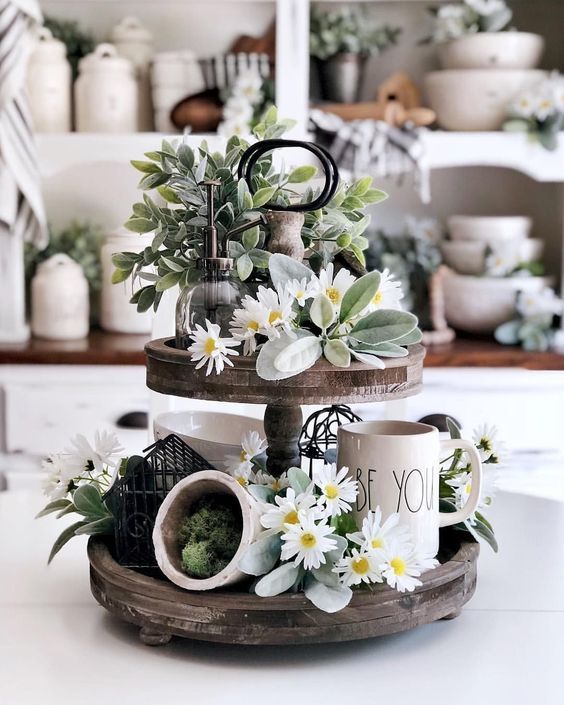 Two-tier wood tray styled with tall greenery, a Be You mug at medium height and low daisies for a varied silhouette