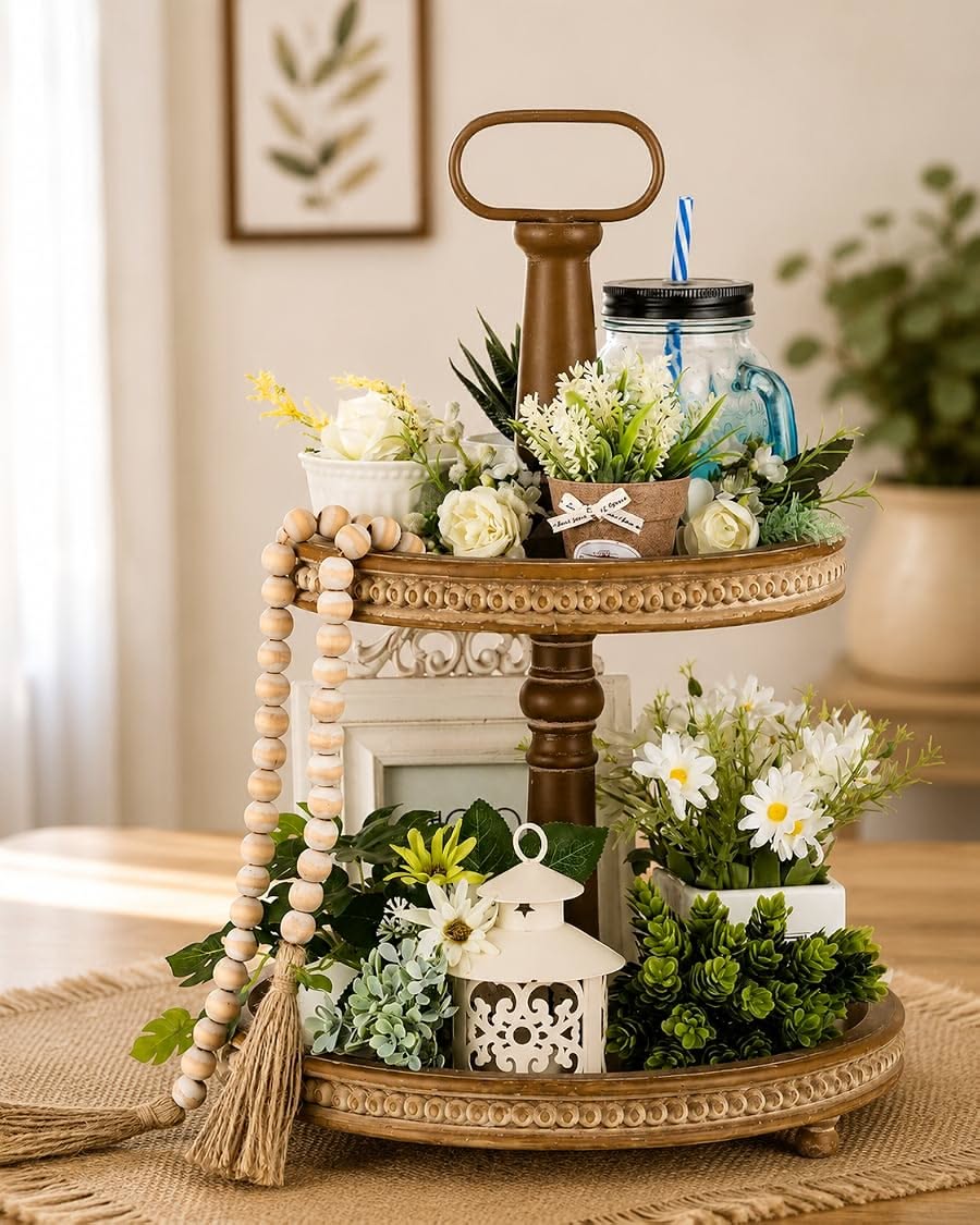 Gold two-tier tray mixing roses, a blue mason jar cup, a white lantern, wood beads and a burlap flower for layered texture