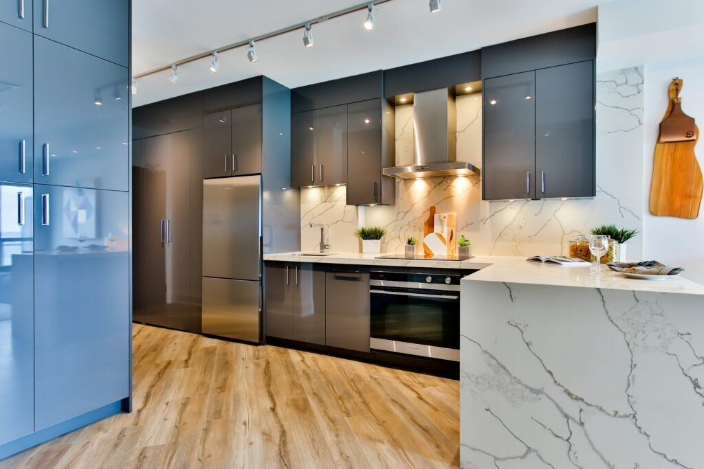 Glossy navy G-shaped kitchen with a marble waterfall peninsula, stainless steel appliances and track lighting