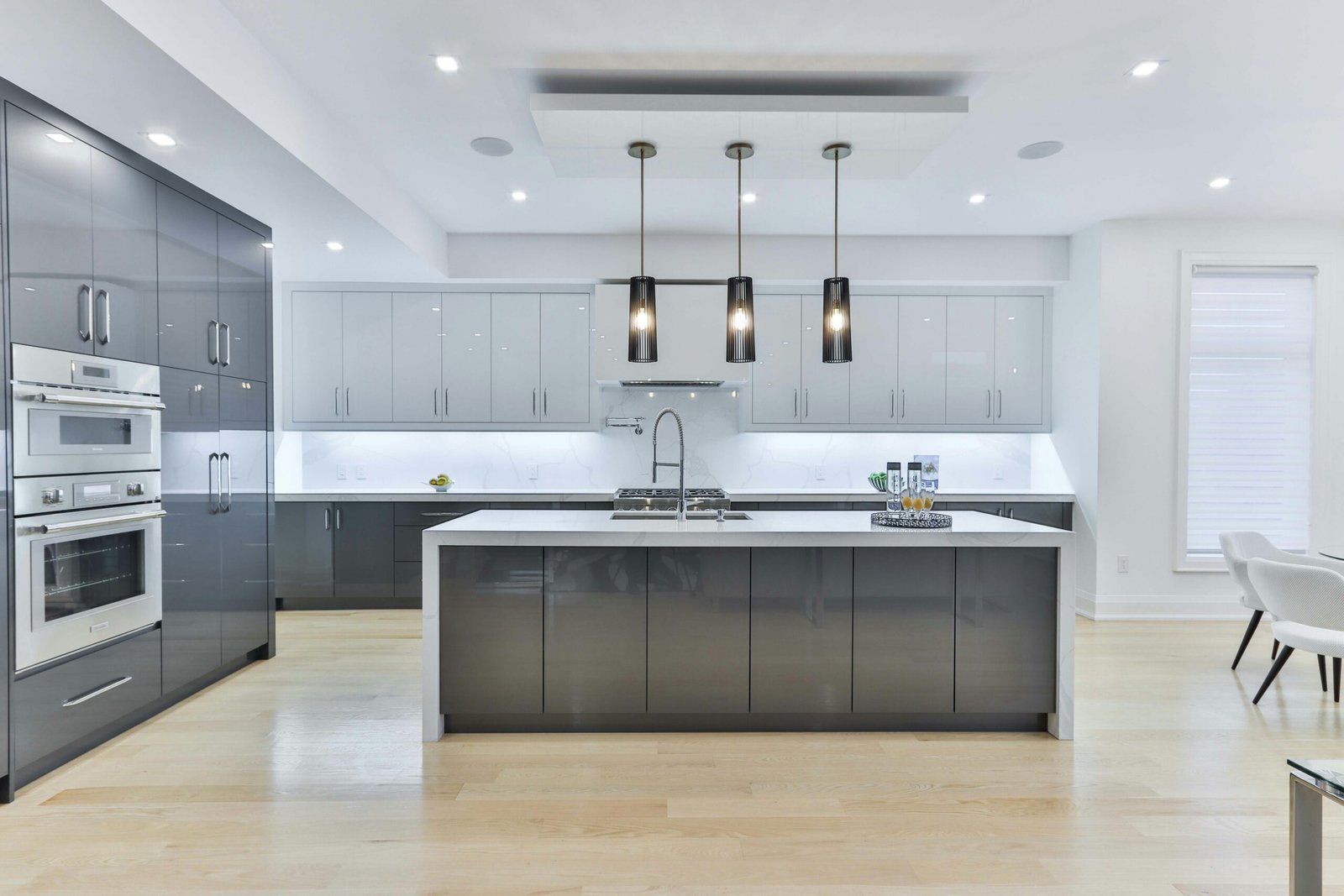 Large modern kitchen with a gray waterfall-edge island, three black pendant lights, glossy gray cabinets and a dining area beyond
