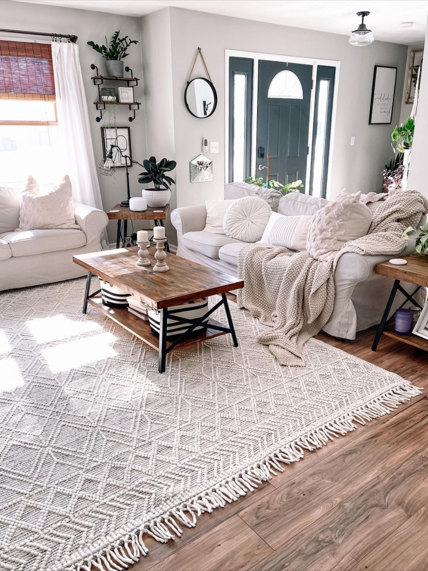 Living room corner with a black-framed mirror, floating shelf, wood side table and layered white and cream decor