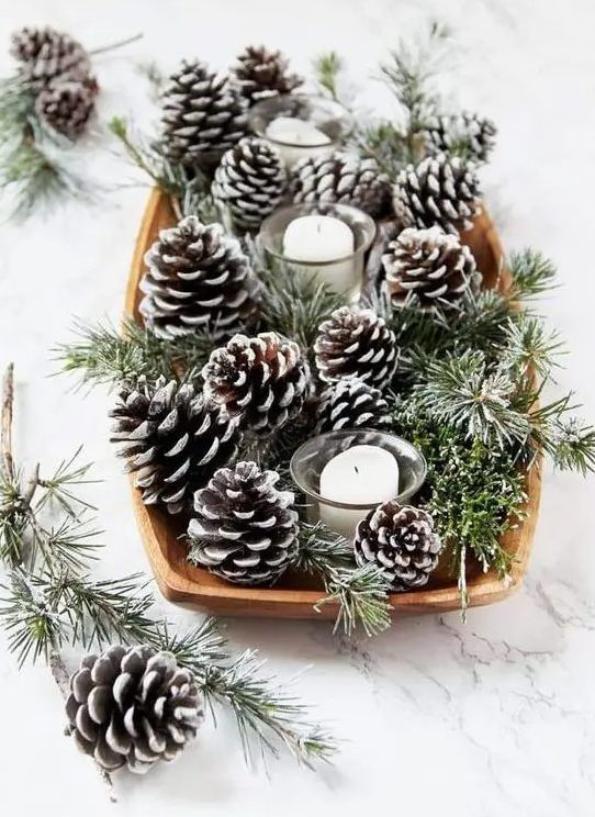 Wood dough bowl filled with snow-dusted frosted pinecones and evergreen sprigs around glass votive candles