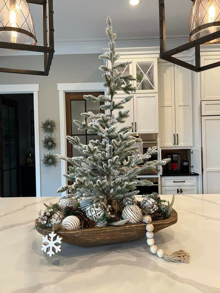 Dough bowl with a single flocked mini tree, wood beads, a snowflake ornament and textured white ornaments on a white kitchen island